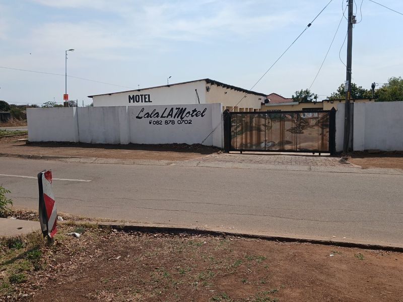 Street view of the motel property featuring a perimeter wall, gated entrance, and prominent business signage.