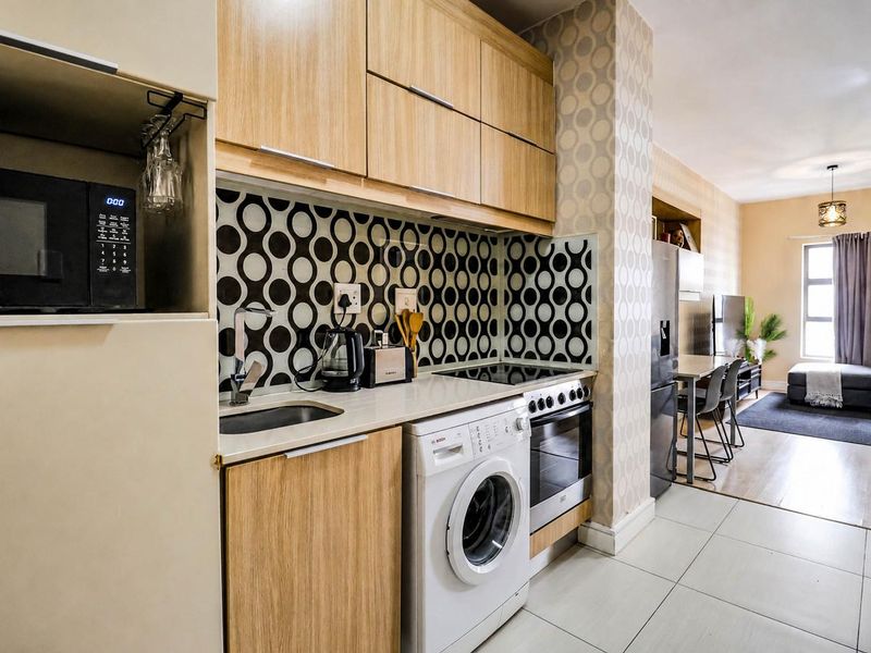 Open-plan kitchen and living area featuring modern wood-finish cabinetry, built-in appliances, and a combination of tiled and laminate flooring.