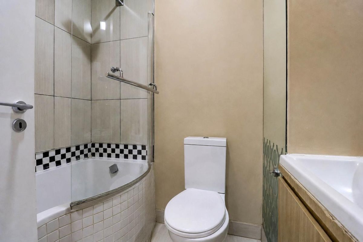 A compact bathroom featuring a bathtub with a glass screen, a standard toilet, and a vanity unit with a basin.