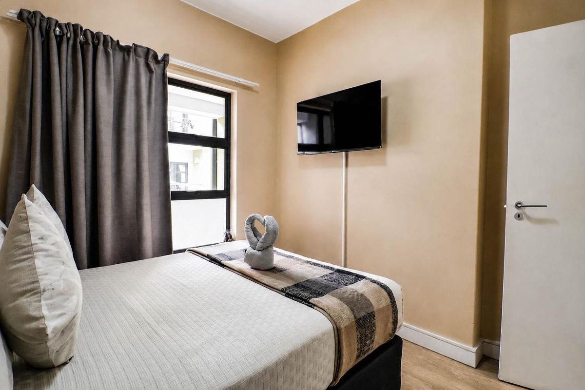 A compact bedroom featuring neutral wall tones, laminate flooring, and an aluminium-framed window with curtaining.