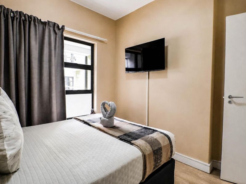A compact bedroom featuring neutral wall tones, laminate flooring, and an aluminium-framed window with curtaining.