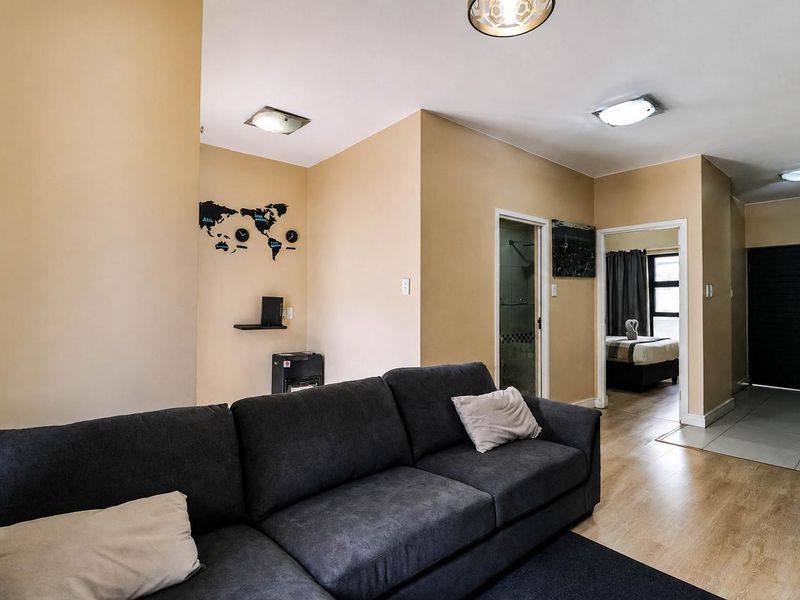 A living room area featuring laminate flooring, neutral wall tones, and access to adjacent rooms, including a bedroom and tiled entryway.