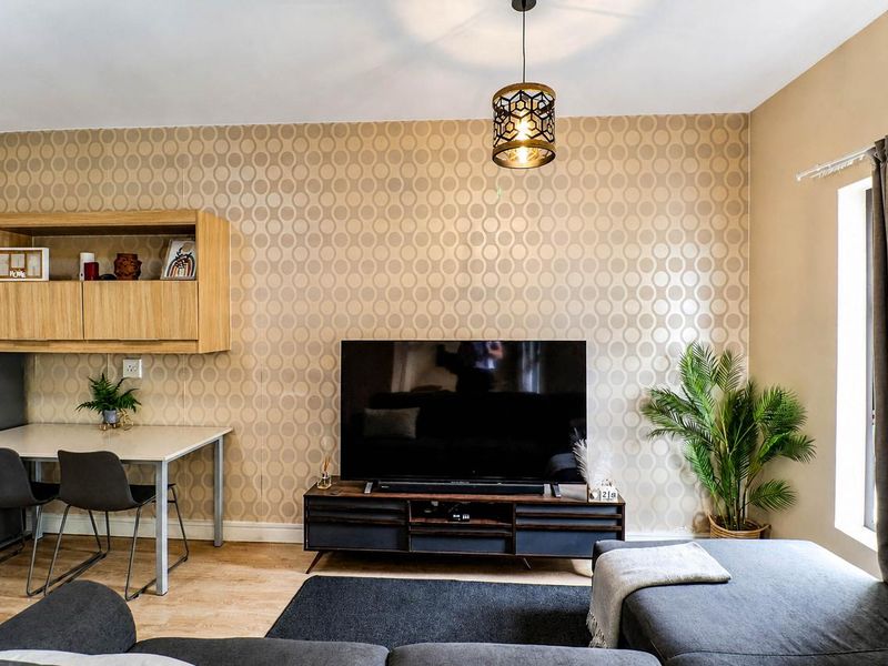 A well-maintained living room featuring patterned wallpaper, laminate flooring, and a modern pendant light fixture.