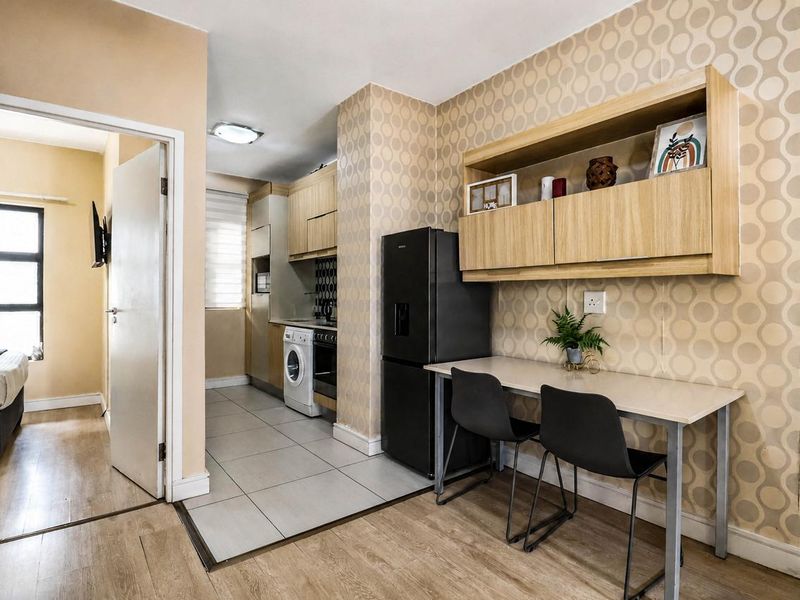 Open-plan kitchen and dining area featuring tiled and laminate flooring, built-in cabinetry, and integrated kitchen appliances, with an adjacent bedroom visible.
