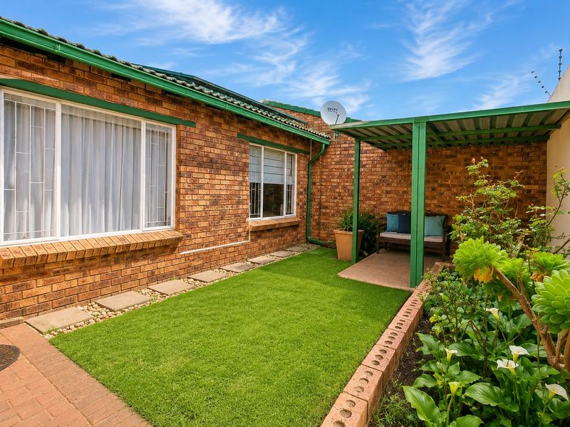 A well-maintained rear courtyard featuring a face brick facade, a small lawn, and a covered patio area with paved pathways.