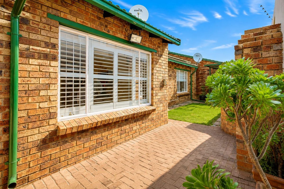 A well-maintained rear exterior view of the townhouse featuring face brick walls, a paved patio area, and white window shutters.