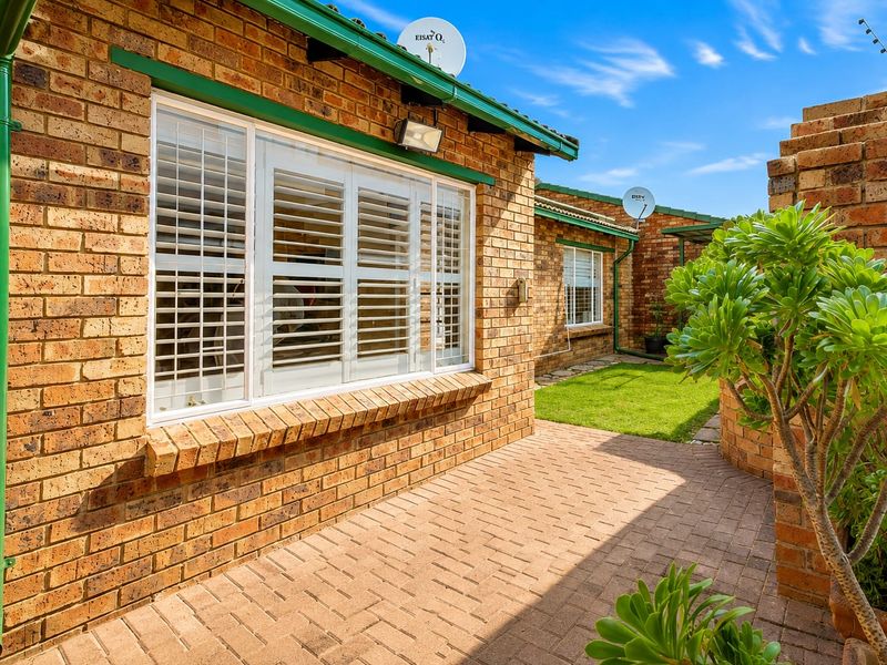 A well-maintained rear exterior view of the townhouse featuring face brick walls, a paved patio area, and white window shutters.