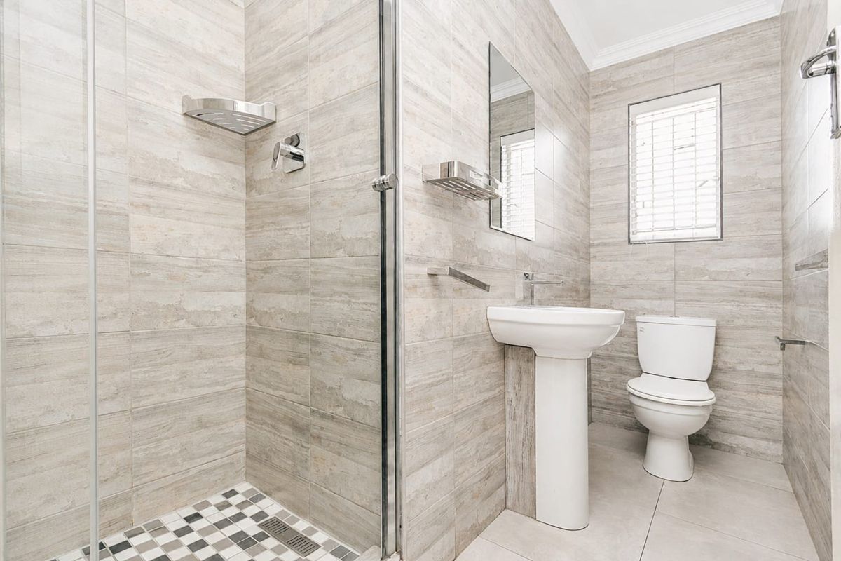 A modern, well-maintained bathroom featuring neutral wall tiles, a glass-enclosed shower, a pedestal sink, and a toilet.