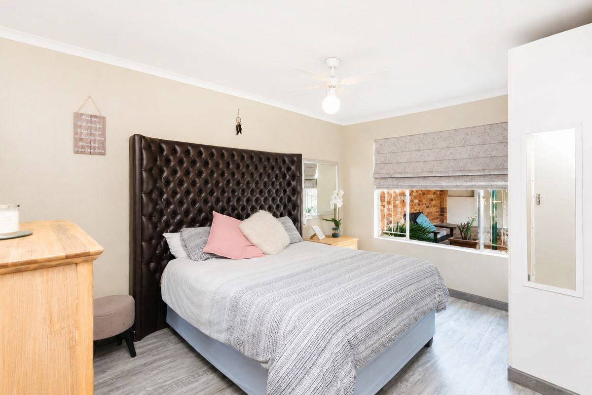 A well-maintained bedroom featuring laminate flooring, a ceiling fan, and a built-in wardrobe with a full-length mirror.