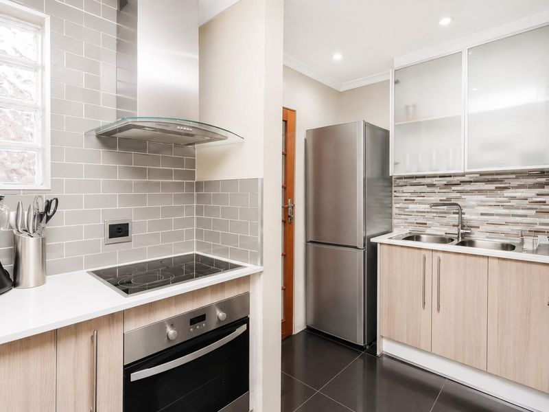 Modern kitchen featuring light wood cabinetry, subway and mosaic tile backsplashes, stainless steel appliances, and a sleek electric cooktop with extractor fan.