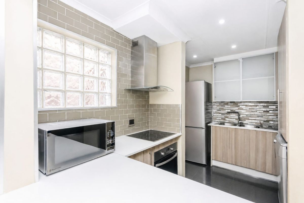 Modern kitchen featuring subway tile backsplash, stainless steel appliances, built-in oven, electric cooktop, and ample cabinetry with frosted glass accents.