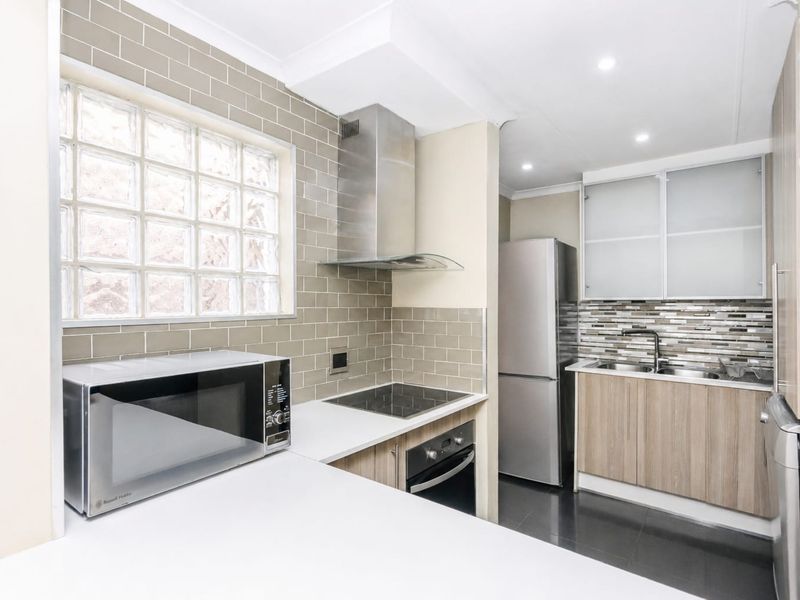 Modern kitchen featuring subway tile backsplash, stainless steel appliances, built-in oven, electric cooktop, and ample cabinetry with frosted glass accents.