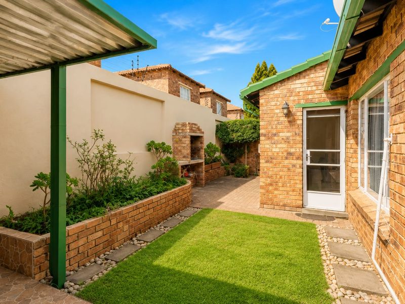 A private rear courtyard featuring a brick-built braai, paved patio area, and established planter boxes, providing a functional outdoor entertainment space.