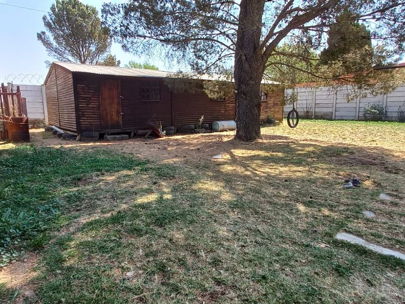A spacious rear garden featuring a large mature tree, a timber outbuilding, and precast concrete boundary walls.