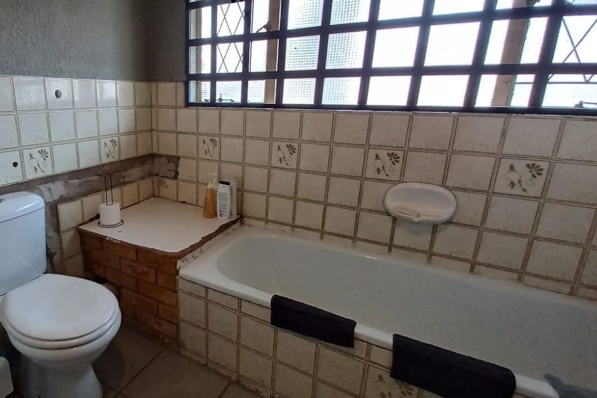 A dated bathroom featuring a bathtub, toilet, and tiled finishes, currently requiring significant repair to the wall tiling and plasterwork.