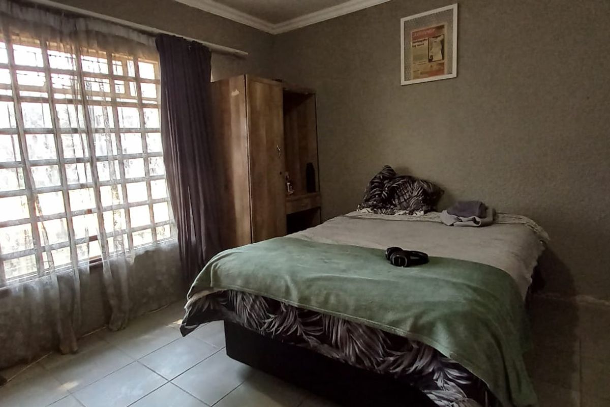 A bedroom featuring tiled flooring, security bars on the window, and textured wall finishes, offering a functional space with potential for cosmetic updates.