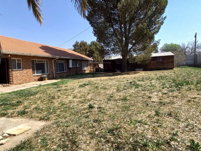 Spacious rear garden featuring a brick-built house with a tiled roof, concrete patio area, and perimeter walling with security spikes.