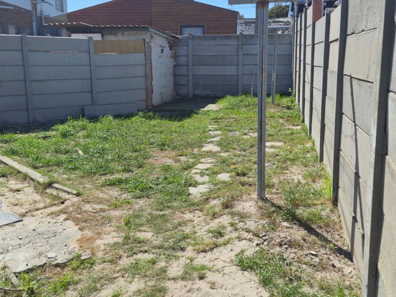 A rear yard area featuring precast concrete boundary walls and a small patch of lawn, requiring landscaping and maintenance to improve its condition.