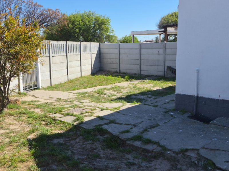 A rear garden area featuring a precast concrete boundary wall and weathered concrete paving, offering potential for landscaping and outdoor improvement.