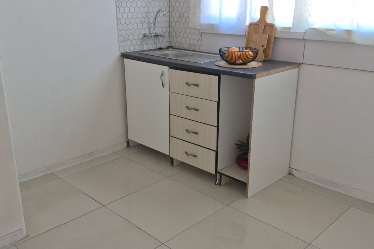 A compact kitchen area featuring a small sink unit, tiled backsplash, and basic cabinetry with an open storage section.