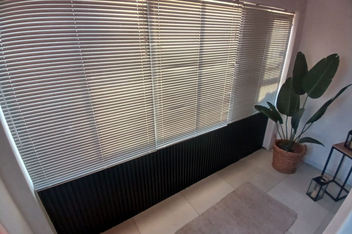 A bright living area featuring modern slatted wall paneling, large windows with venetian blinds, and neutral tiled flooring.