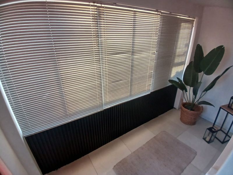 A bright living area featuring modern slatted wall paneling, large windows with venetian blinds, and neutral tiled flooring.