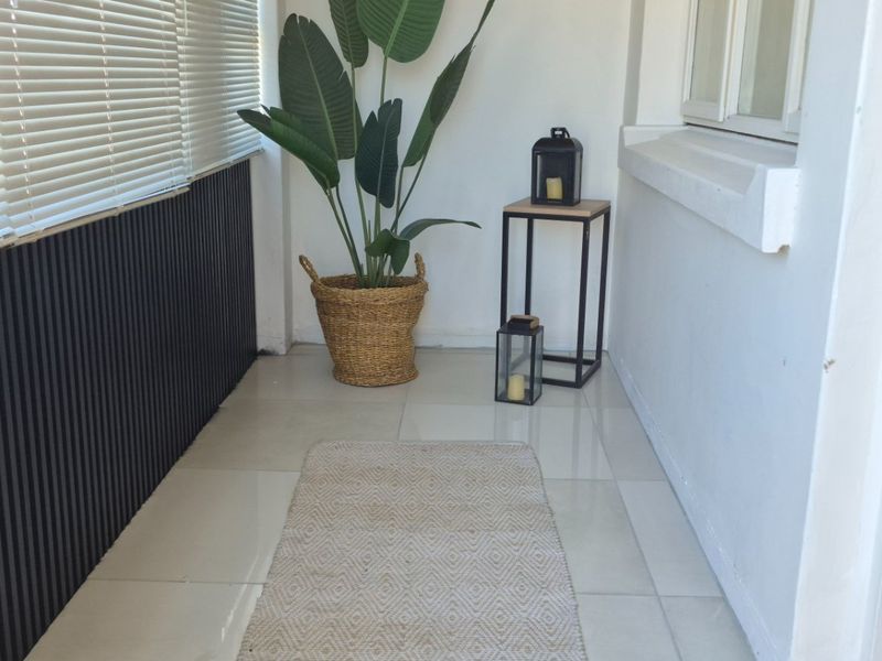 A covered balcony or patio area featuring tiled flooring, slatted wall paneling, and venetian blinds, secured by a metal gate.