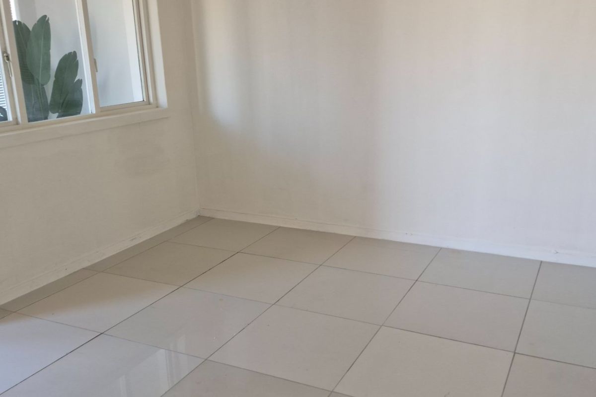 A bright, empty bedroom featuring neutral tiled flooring and a large sliding window, providing a clean canvas for personalization.