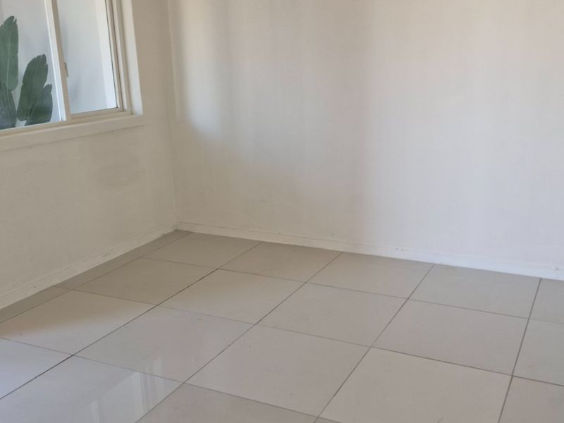 A bright, empty bedroom featuring neutral tiled flooring and a large sliding window, providing a clean canvas for personalization.
