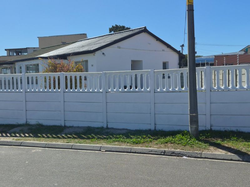 Front view of a residential property featuring a white precast concrete boundary wall with integrated electric fencing and a metal pedestrian gate.