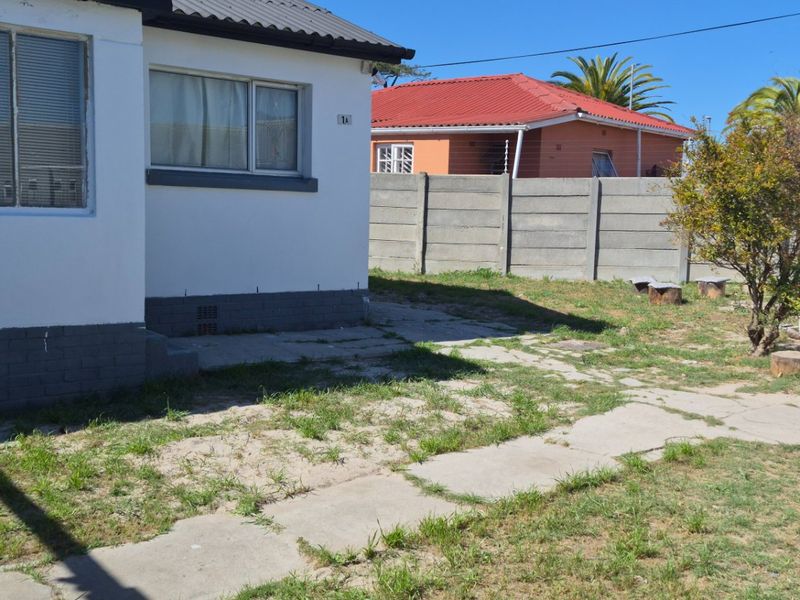 Rear exterior view of the property featuring a paved area, lawn, and concrete boundary walling.