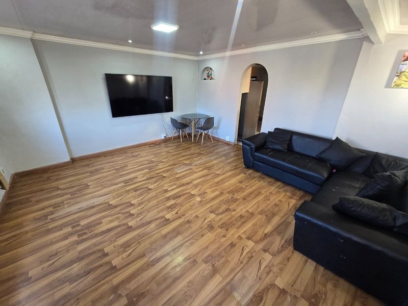 Spacious living room featuring wood-look laminate flooring, coved ceilings, and a distinctive arched doorway leading to an adjacent area.