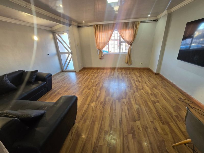 A spacious living room featuring laminate wood flooring, crown molding, and recessed lighting, with a security gate providing access to the exterior.