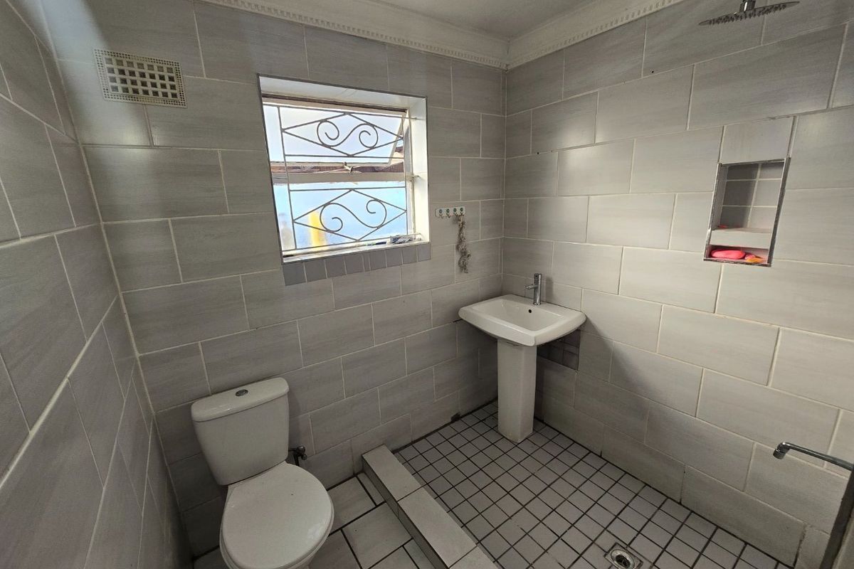A functional bathroom featuring a pedestal basin, toilet, and a walk-in shower area with a recessed niche and neutral wall tiling.