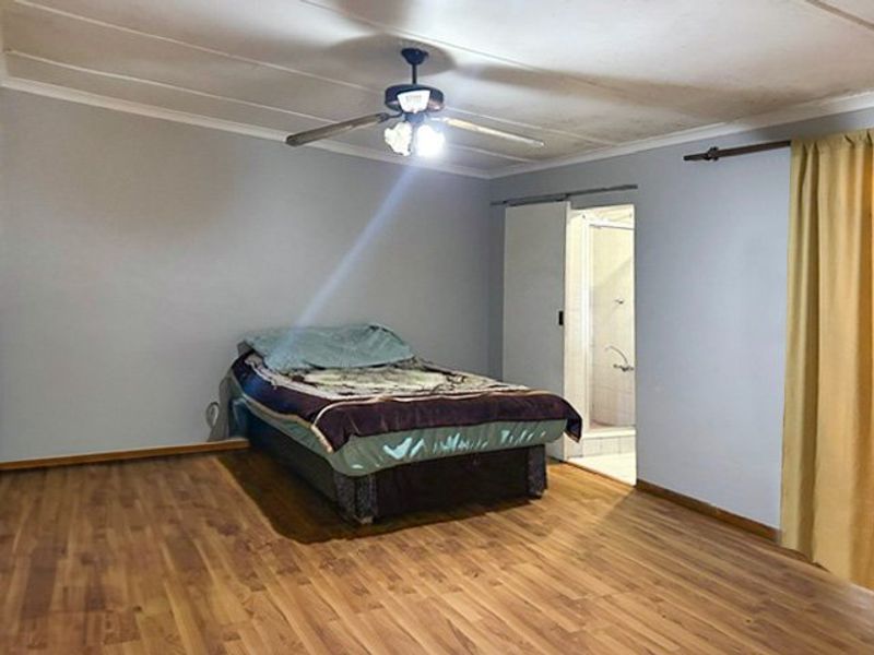A bedroom featuring laminate flooring, a ceiling fan, and direct access to an en-suite bathroom.
