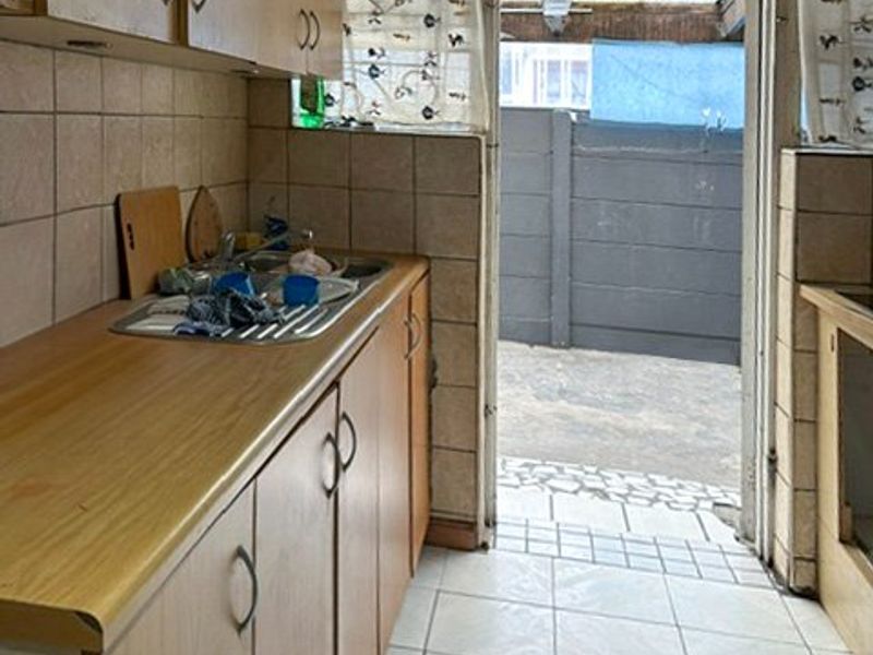 A functional kitchen featuring laminate countertops, built-in cabinetry, and tiled finishes, with direct access to an outdoor patio area.