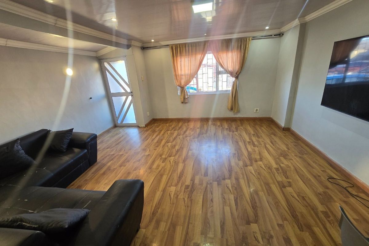 A living room featuring laminate wood flooring, recessed ceiling lighting, and security features on the window and entrance door.