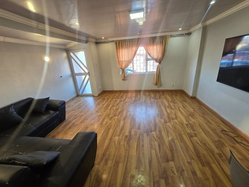 A living room featuring laminate wood flooring, recessed ceiling lighting, and security features on the window and entrance door.