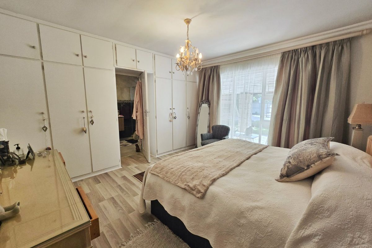 A well-maintained bedroom featuring extensive built-in cupboards, laminate flooring, and direct access to an en-suite bathroom.