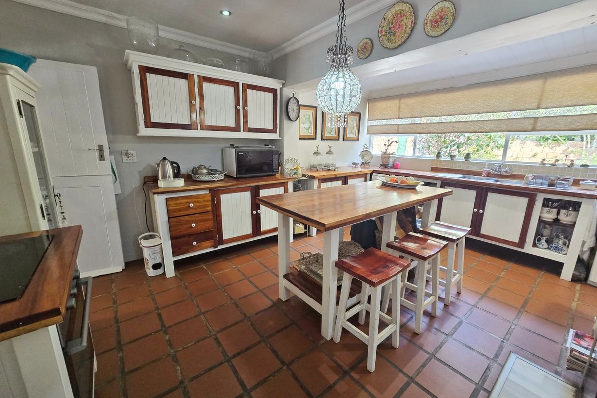 A rustic-style kitchen featuring wooden countertops, white and wood-toned cabinetry, terracotta tiled flooring, and a central island with integrated seating.