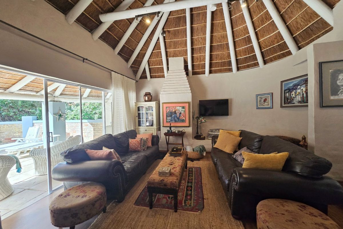 Spacious living room featuring a high vaulted thatched ceiling with exposed timber rafters, a central masonry fireplace, and large sliding doors opening to the patio.
