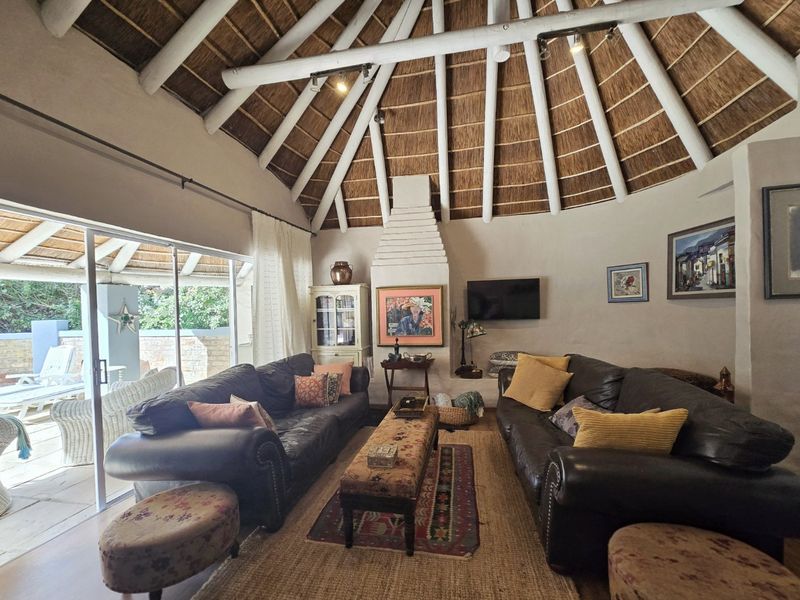 Spacious living room featuring a high vaulted thatched ceiling with exposed timber rafters, a central masonry fireplace, and large sliding doors opening to the patio.