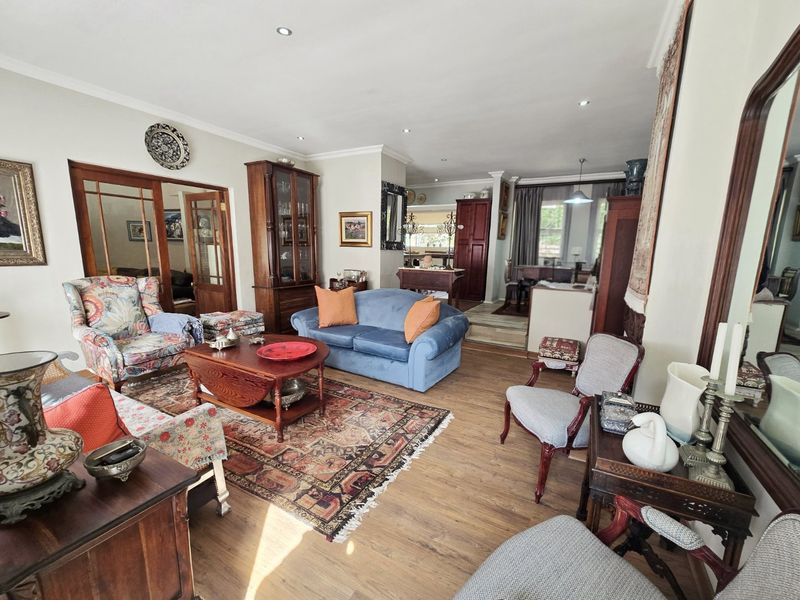 Spacious open-plan living and dining area featuring timber laminate flooring, recessed lighting, and classic timber-framed glass doors connecting to adjacent rooms.