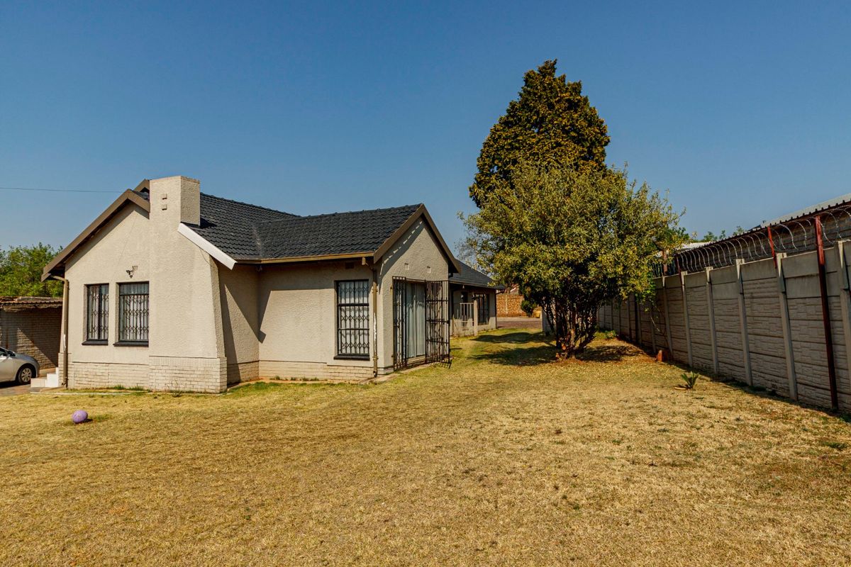 Rear view of the house featuring a tiled roof, security bars on windows, and a fenced perimeter with razor wire.