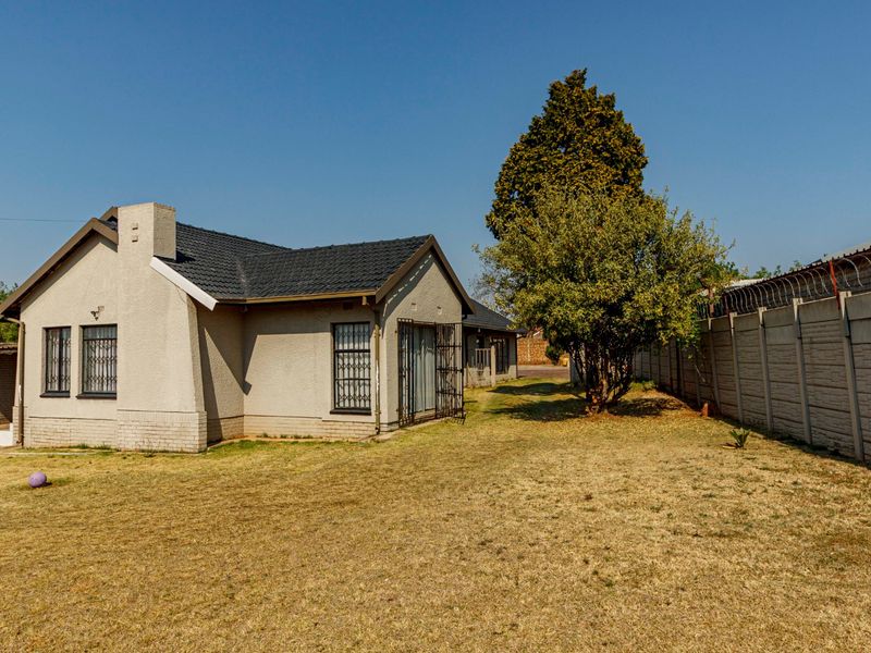 Rear view of the house featuring a tiled roof, security bars on windows, and a fenced perimeter with razor wire.