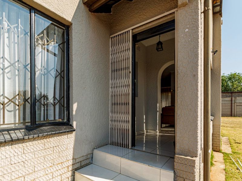 Entrance area featuring tiled steps, a security gate, and textured exterior wall finish with security bars on the adjacent window.