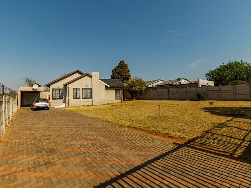 Front view of the property featuring a long paved driveway, a carport, and a spacious front garden enclosed by a precast boundary wall.