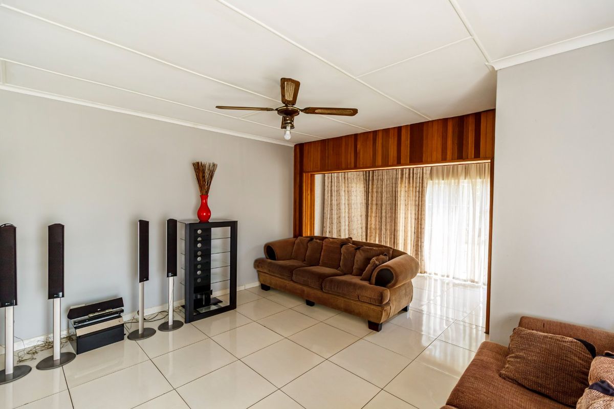 A living room featuring tiled flooring, a ceiling fan, and timber wall paneling, with access to an outdoor area through sliding glass doors.