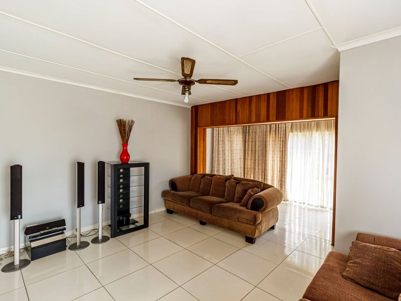 A living room featuring tiled flooring, a ceiling fan, and timber wall paneling, with access to an outdoor area through sliding glass doors.