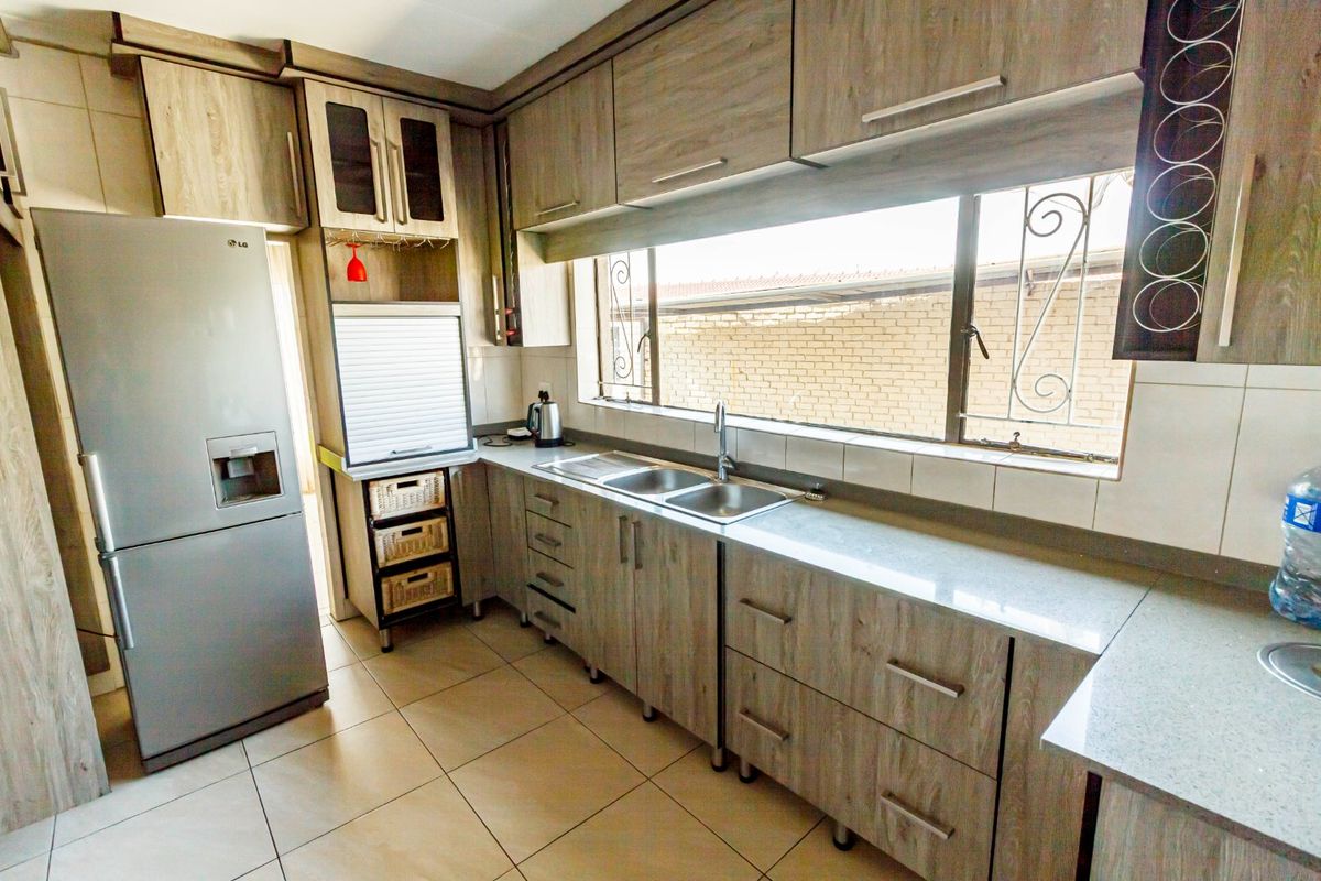 A functional kitchen featuring wood-look laminate cabinetry, stone countertops, a double basin sink, and tiled flooring with natural light from a large window.
